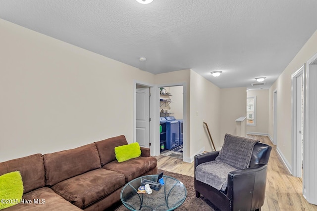 living room with washer and dryer, a textured ceiling, and light hardwood / wood-style floors