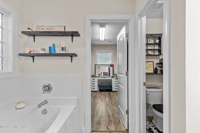 bathroom with wood-type flooring, toilet, a textured ceiling, and a washtub