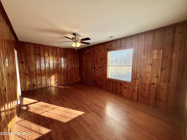 empty room featuring ceiling fan, ornamental molding, hardwood / wood-style floors, and wood walls