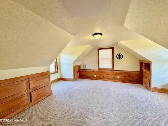 bonus room featuring lofted ceiling, light carpet, and a textured ceiling