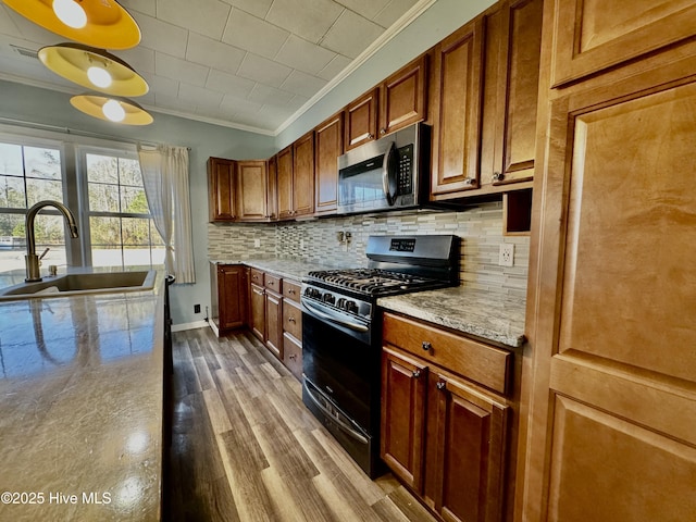 kitchen with appliances with stainless steel finishes, tasteful backsplash, sink, hardwood / wood-style flooring, and ornamental molding