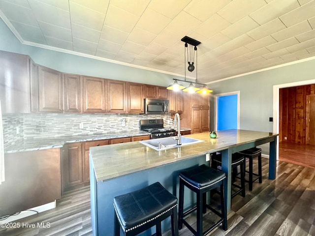 kitchen with an island with sink, sink, hanging light fixtures, range, and dark wood-type flooring