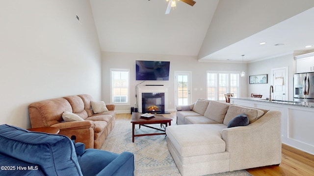 living room featuring ceiling fan, sink, high vaulted ceiling, and light hardwood / wood-style flooring