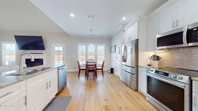 kitchen with sink, white cabinetry, pendant lighting, stainless steel appliances, and light stone countertops