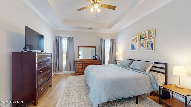 bedroom featuring a raised ceiling, crown molding, ceiling fan, and light hardwood / wood-style floors