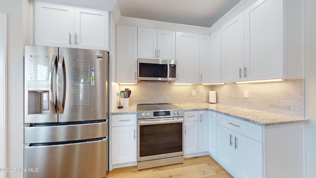 kitchen with white cabinetry, backsplash, stainless steel appliances, and light stone countertops