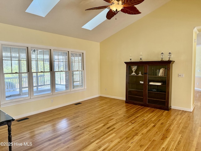 unfurnished living room with visible vents, light wood-style floors, ceiling fan, vaulted ceiling with skylight, and baseboards