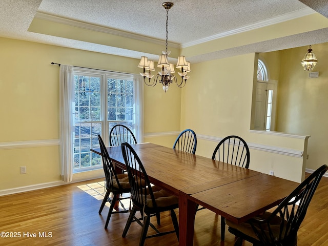 dining room with a textured ceiling, ornamental molding, wood finished floors, and a notable chandelier