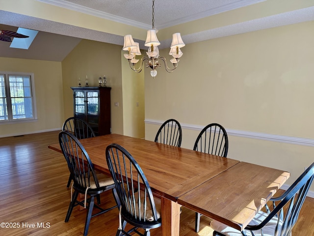 dining room with vaulted ceiling with skylight, a textured ceiling, a chandelier, and wood finished floors