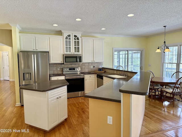 kitchen with stainless steel appliances, a peninsula, a sink, light wood-type flooring, and dark countertops