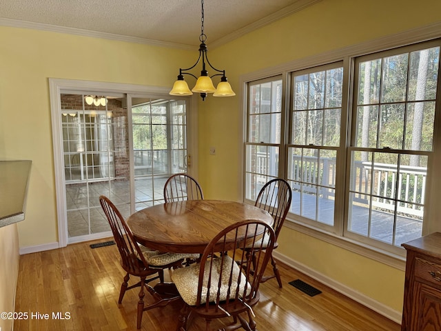 dining area with light wood-style flooring, visible vents, a textured ceiling, and ornamental molding