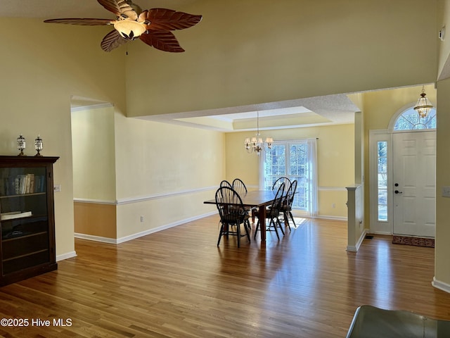 dining area featuring ceiling fan with notable chandelier, a raised ceiling, wood finished floors, and baseboards