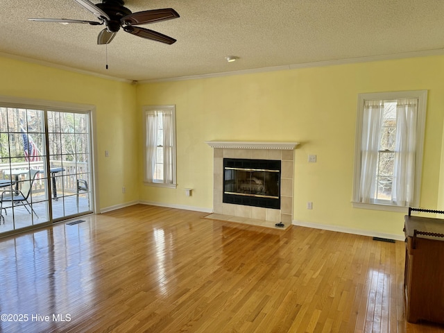 unfurnished living room with crown molding, visible vents, a tiled fireplace, a textured ceiling, and wood finished floors