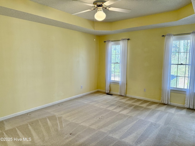 empty room featuring visible vents, light colored carpet, a ceiling fan, a textured ceiling, and baseboards