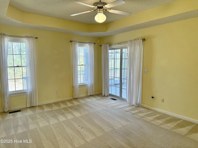 empty room with light carpet, a tray ceiling, and a textured ceiling