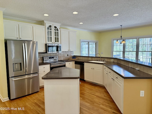 kitchen with dark countertops, light wood-style flooring, appliances with stainless steel finishes, a peninsula, and a sink