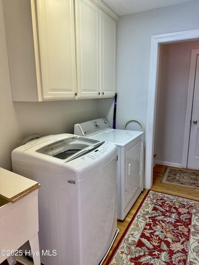 washroom with cabinet space, light wood finished floors, and washer and dryer