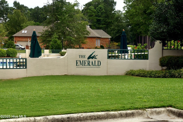 community / neighborhood sign featuring fence and a lawn