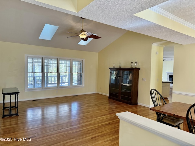 living room featuring a ceiling fan, lofted ceiling with skylight, a textured ceiling, wood finished floors, and baseboards