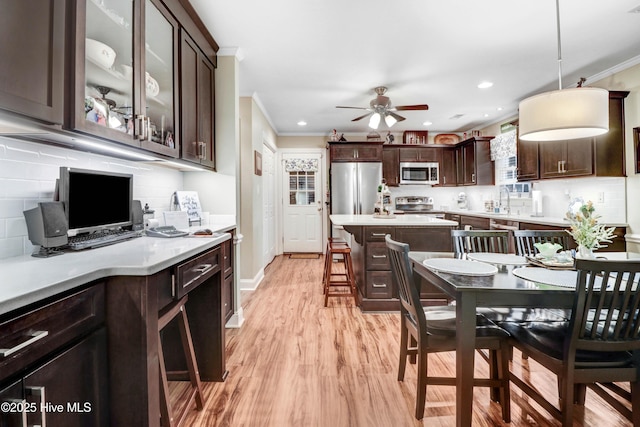 kitchen with appliances with stainless steel finishes, pendant lighting, a breakfast bar area, ornamental molding, and dark brown cabinetry