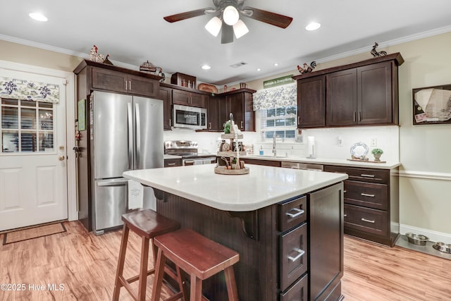 kitchen with crown molding, appliances with stainless steel finishes, dark brown cabinets, a kitchen breakfast bar, and a center island