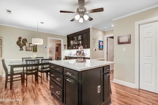 kitchen with hanging light fixtures, ornamental molding, a center island, light hardwood / wood-style floors, and dark brown cabinets