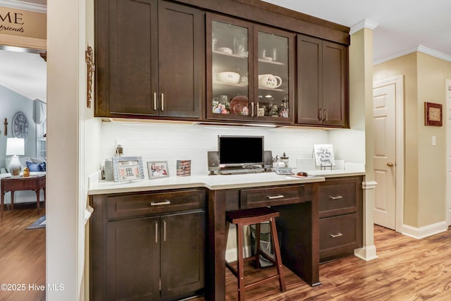 bar featuring light hardwood / wood-style flooring, backsplash, dark brown cabinets, and ornamental molding