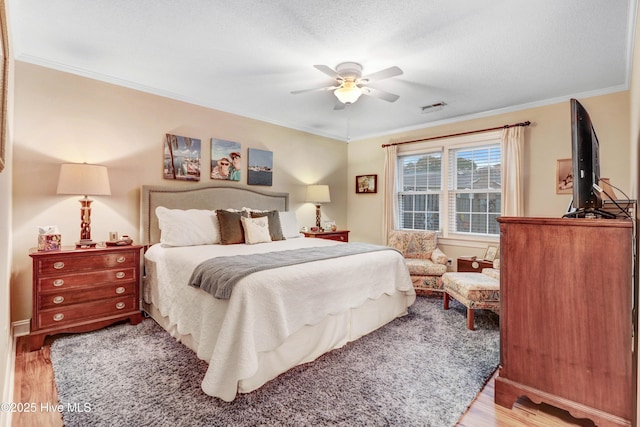 bedroom featuring hardwood / wood-style flooring, ornamental molding, ceiling fan, and a textured ceiling