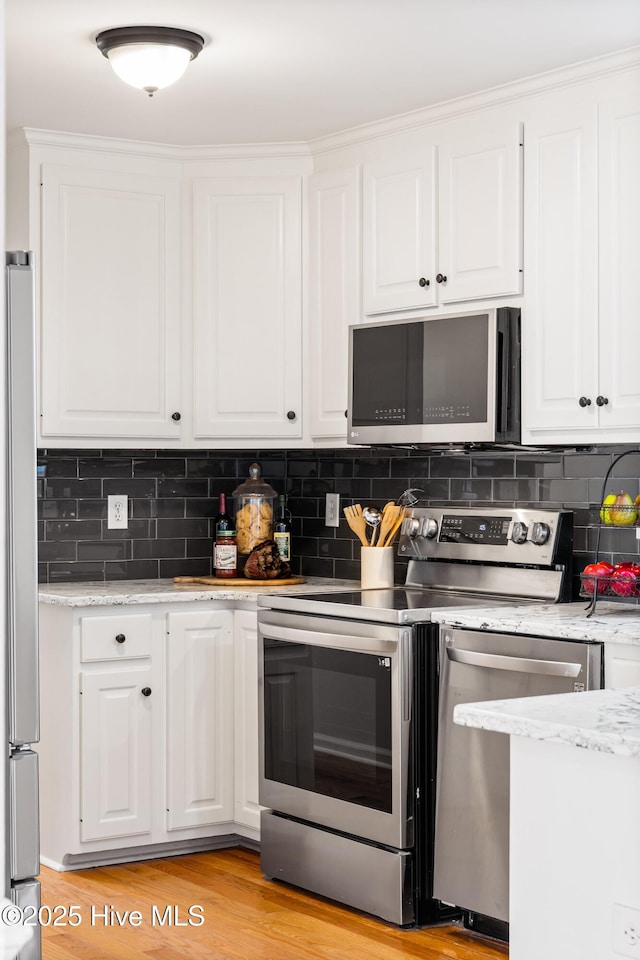 kitchen featuring light stone counters, light hardwood / wood-style flooring, appliances with stainless steel finishes, white cabinets, and backsplash