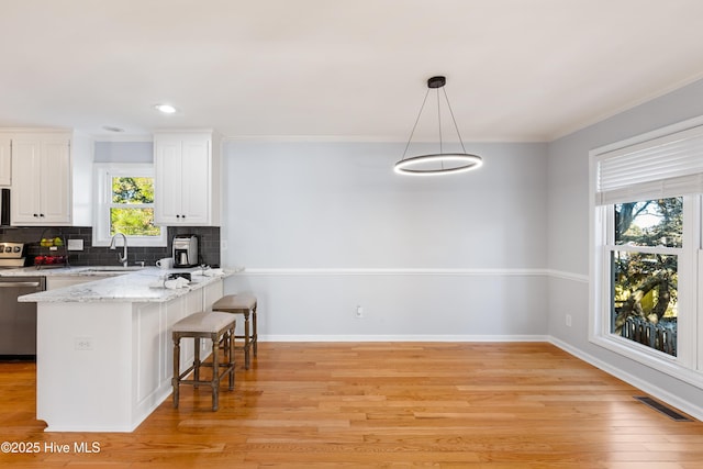 kitchen with white cabinetry, decorative light fixtures, stainless steel dishwasher, a kitchen breakfast bar, and kitchen peninsula