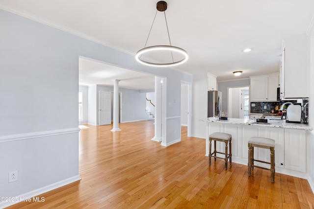 kitchen featuring stainless steel refrigerator, white cabinetry, light stone counters, crown molding, and light wood-type flooring