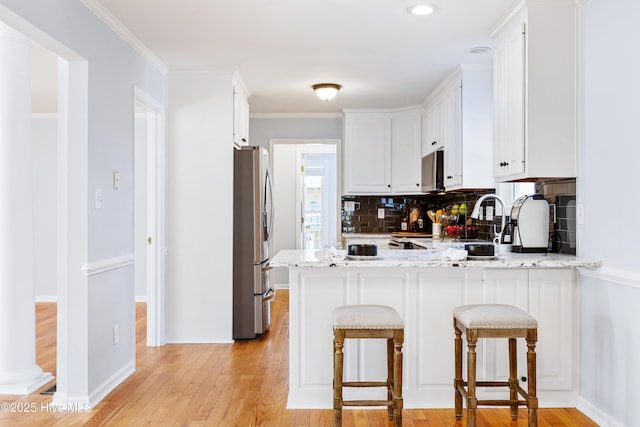 kitchen with a kitchen bar, light stone counters, appliances with stainless steel finishes, kitchen peninsula, and white cabinets