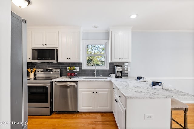 kitchen with sink, stainless steel appliances, white cabinets, a kitchen bar, and kitchen peninsula