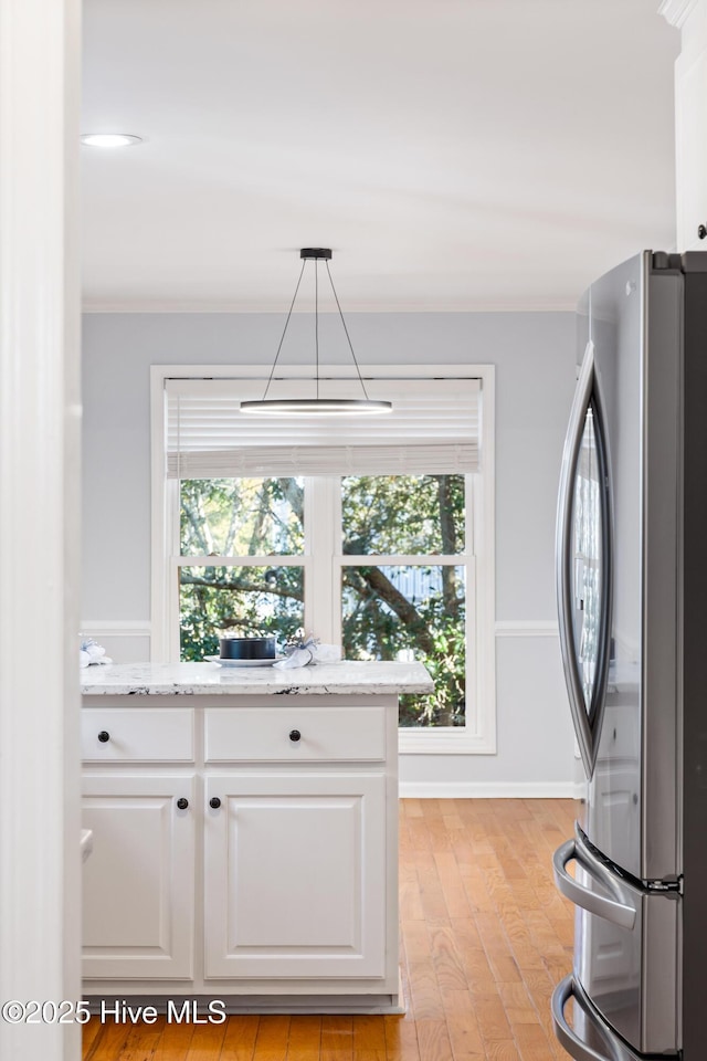 kitchen with crown molding, hanging light fixtures, stainless steel refrigerator, light stone countertops, and white cabinets