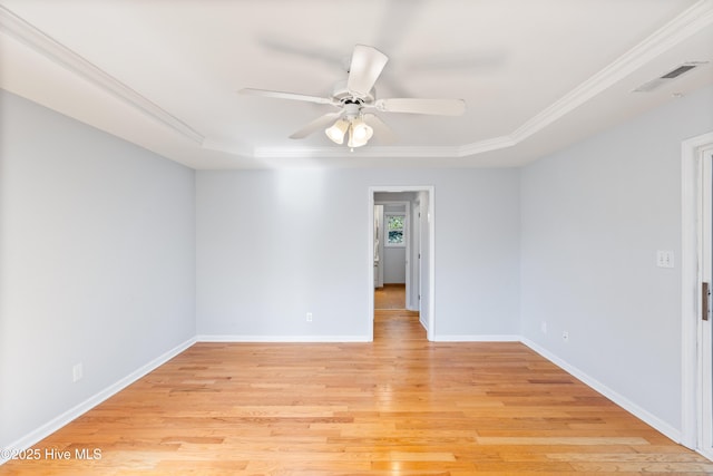 empty room with a tray ceiling, light hardwood / wood-style flooring, ornamental molding, and ceiling fan