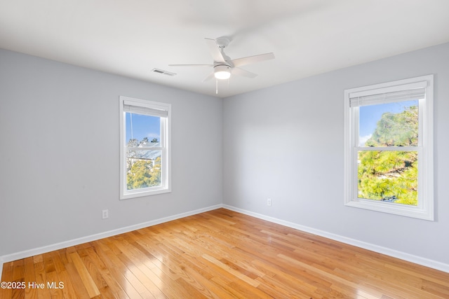 empty room with ceiling fan, a wealth of natural light, and light wood-type flooring