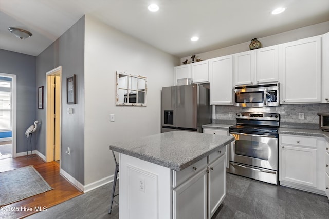 kitchen with appliances with stainless steel finishes, dark hardwood / wood-style floors, white cabinets, decorative backsplash, and a center island