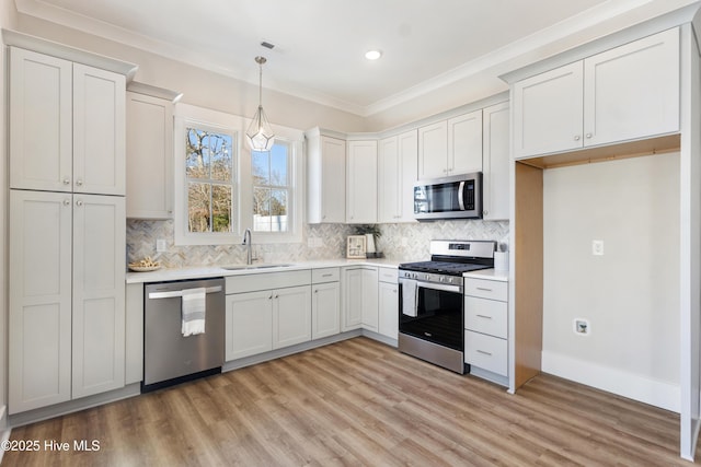 kitchen with sink, appliances with stainless steel finishes, hanging light fixtures, ornamental molding, and white cabinets