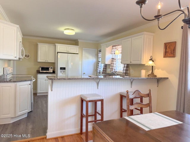 kitchen with dark stone countertops, white cabinets, white appliances, and kitchen peninsula