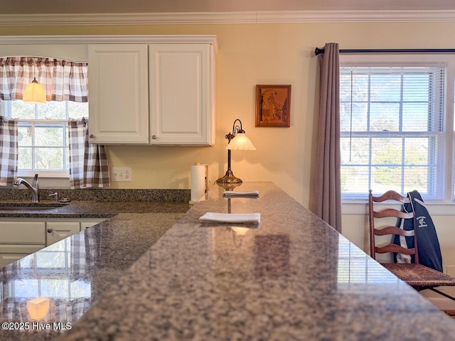 kitchen with ornamental molding, sink, dark stone countertops, and white cabinets