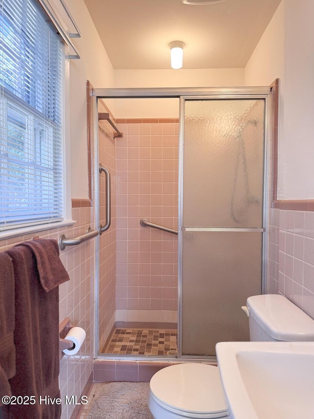 bathroom with tile walls, a shower with shower door, and toilet