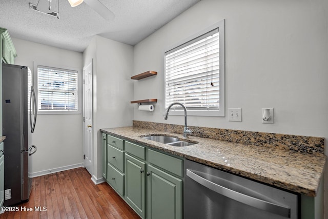 kitchen with sink, light stone counters, light hardwood / wood-style flooring, a textured ceiling, and appliances with stainless steel finishes