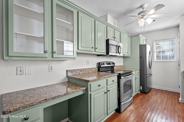 kitchen featuring stainless steel appliances, light wood-type flooring, green cabinets, and a textured ceiling