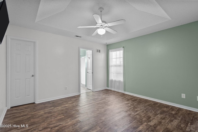 spare room with ceiling fan, a tray ceiling, dark hardwood / wood-style floors, and a textured ceiling