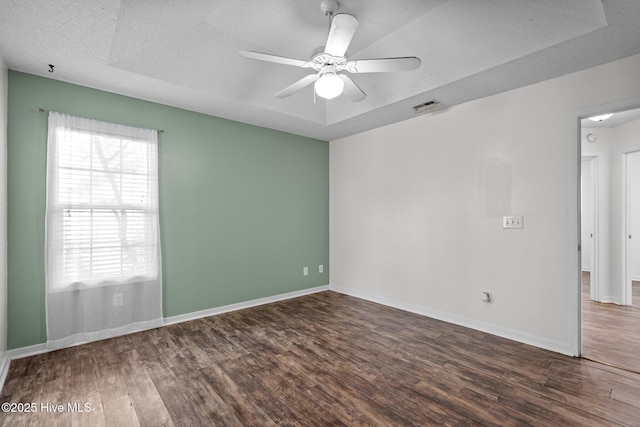 spare room featuring dark wood-type flooring, ceiling fan, a tray ceiling, and a textured ceiling