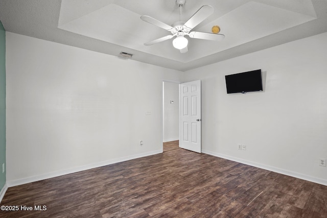 empty room featuring a raised ceiling, ceiling fan, and dark hardwood / wood-style flooring