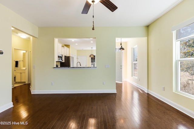 unfurnished living room with plenty of natural light, dark wood-type flooring, and ceiling fan