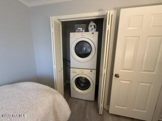 laundry area featuring stacked washer / drying machine, laundry area, crown molding, and dark wood-style flooring