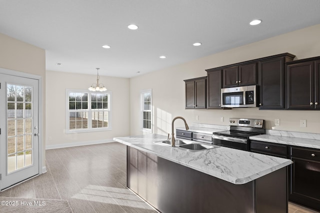 kitchen with dark brown cabinetry, sink, decorative light fixtures, appliances with stainless steel finishes, and an island with sink