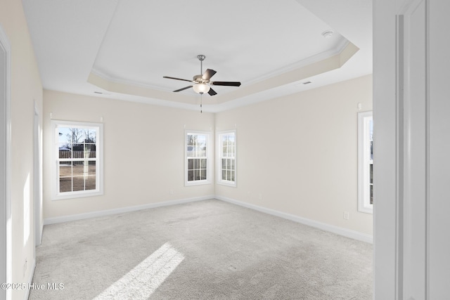 spare room featuring a raised ceiling, ornamental molding, light colored carpet, and ceiling fan